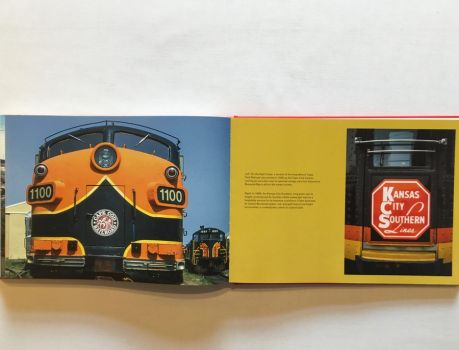 In this colour photograph taken by the railfan designer Ian Logan, the nose of a diesel locomotive is painted in Cape Cod Railroad livery, an orange body overlaid with a scalloped, yellow-edged black waistband and a central roundel carrying the company name in white serif capitals, a floral flourish on a red background at its centre.