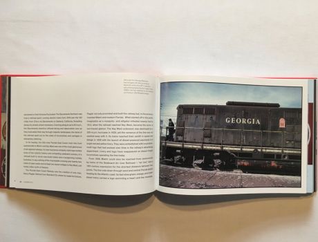In this colour photograph taken by Ian Logan in the 1980s a GP 7 diesel locomotive of the Georgia Railroad inches forward with a lookout standing on the forward platform. Painted dark grey, it carries the name Georgia painted in white serif capitals and the badge of the Georgia Railroad with three white pillars on a red background labelled Courtesy, Safety and Service supporting a lintel and arch emblazoned with the name Georgia RR, Old Reliable.