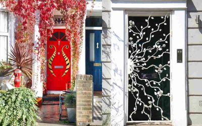 These photographs of two doors side by side were taken by Cath Harries. The door on the left is red with a gold pattern and red leaves hanging over it. The door on the right is black with white wrought-iron tendrils snaking across it and is bordered by white frame.