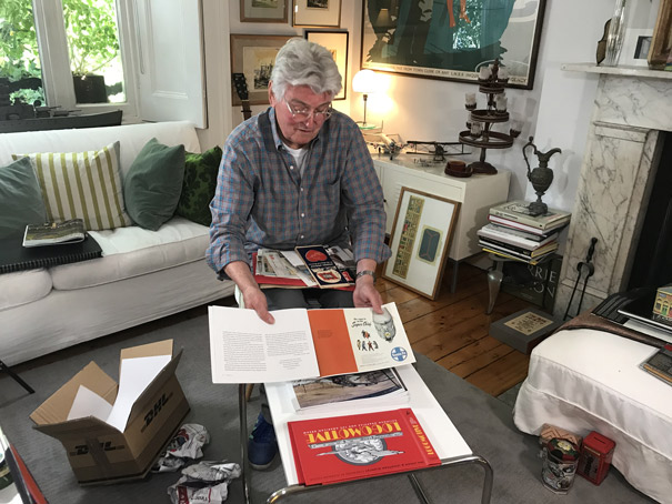 Colour photograph of a big moment when the designer Ian Logan, seated in his sitting room, sees the printed proofs of his book Logomotive for the first time.