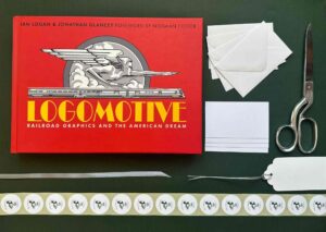 In this colour photograph a copy of ‘Logomotive’, its cover ablaze with red and yellow, rests upon sage green Kraft paper alongside miniature envelopes, gift tags, silver ribbon and Sheldrake Press branded labels.