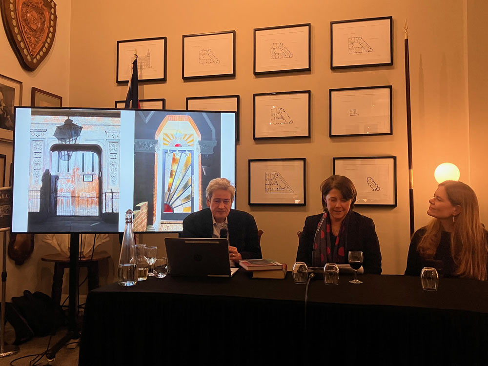In this colour photograph Chris Schüler, Cath Harries and Melanie Backe-Hansen sit at a table with microphones and show illustrations from ‘Doors of London’ on a large screen.