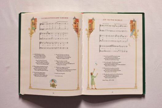 An illuminated double-page spread from A Book of Christmas Carols carries the words and music of A Child This Day Is Born and Joy to The World.